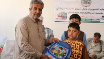 دانشآموز در حال دریافت کیف و لوازمالتحریر از مؤسسه خیریه امام جواد (ع) در سال تعلیمی ۱۴۰۵